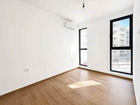 Prazna soba sa bijelim zidovima, drvenim podom, klima uređajem i prozorima. - image 14