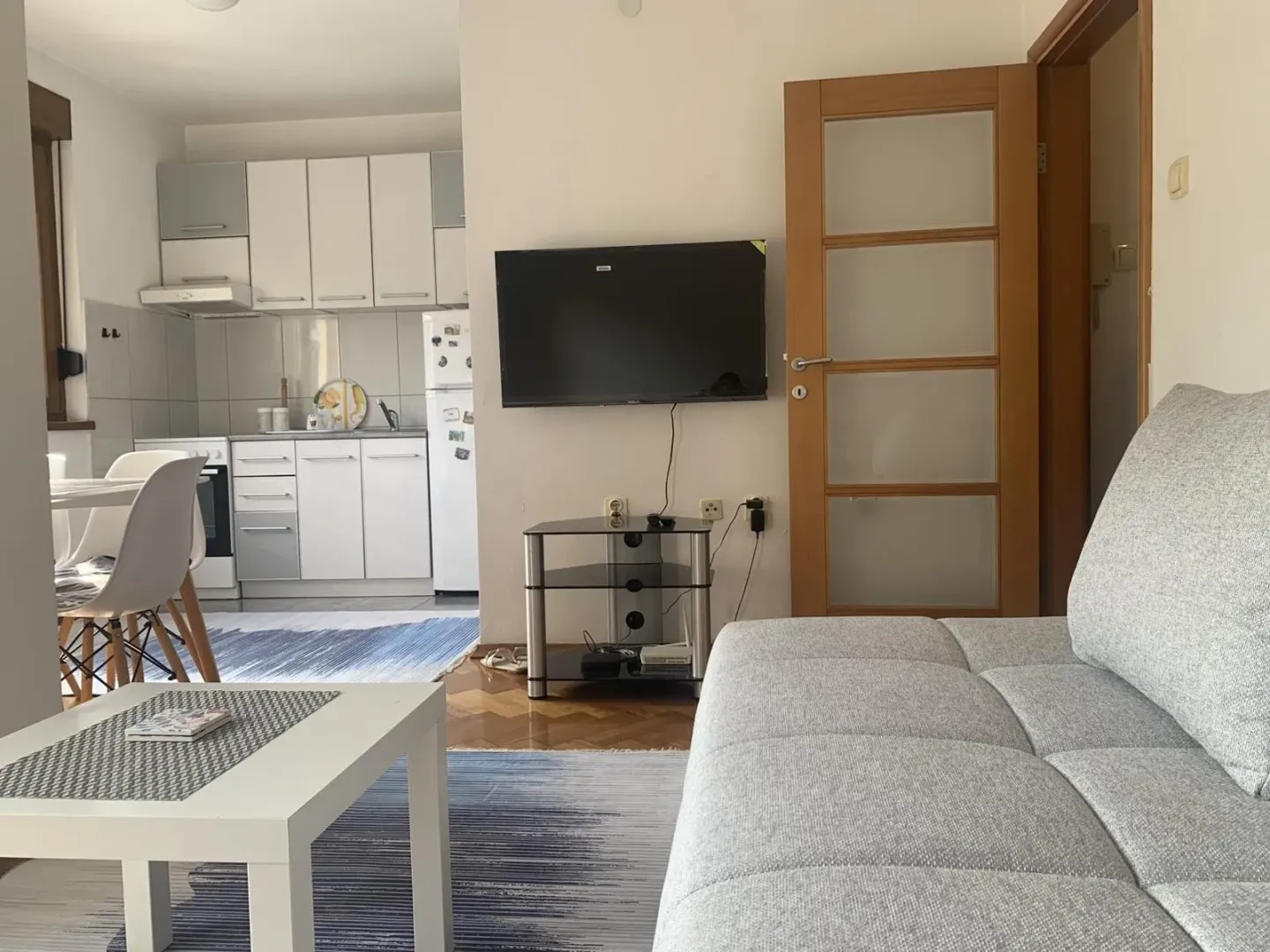 Svijetla dnevna soba sa garniturom za sjedjenje spojena sa kuhinjom.