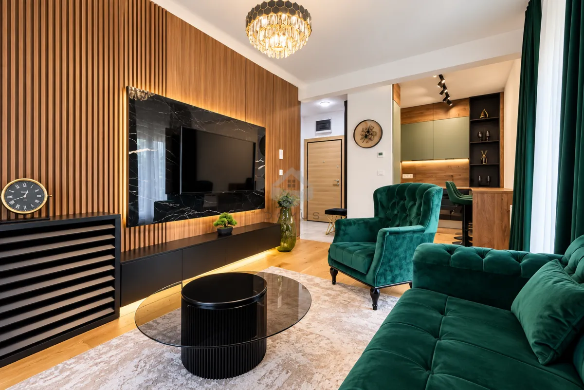 Modern living room with green sofa, wooden wall panels and a view of the kitchen.