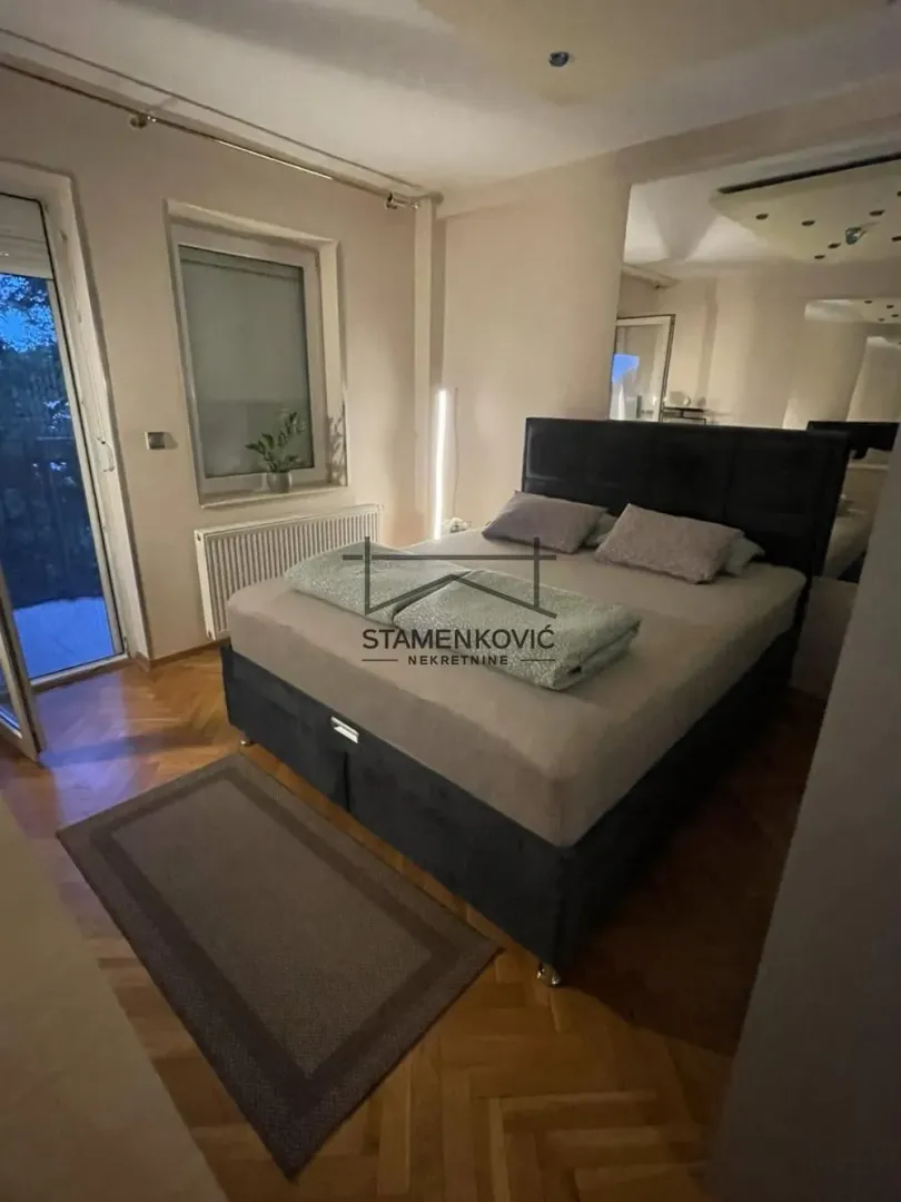 Spavaća soba sa bračnim krevetom, parketom na podu i izlazom na terasu.