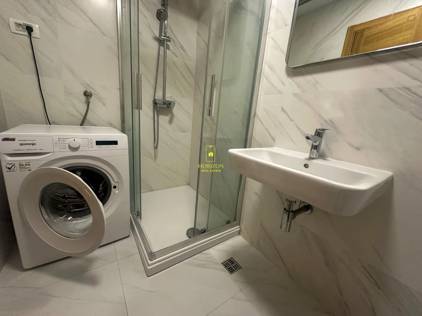 Moderne kupatilo sa tuš kabinom, umivaonikom i veš mašinom.