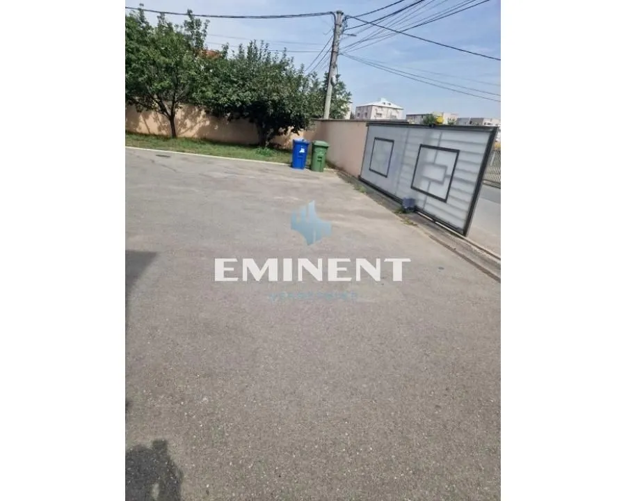 Asfaltirano dvorište sa kapijom i zelenilom.