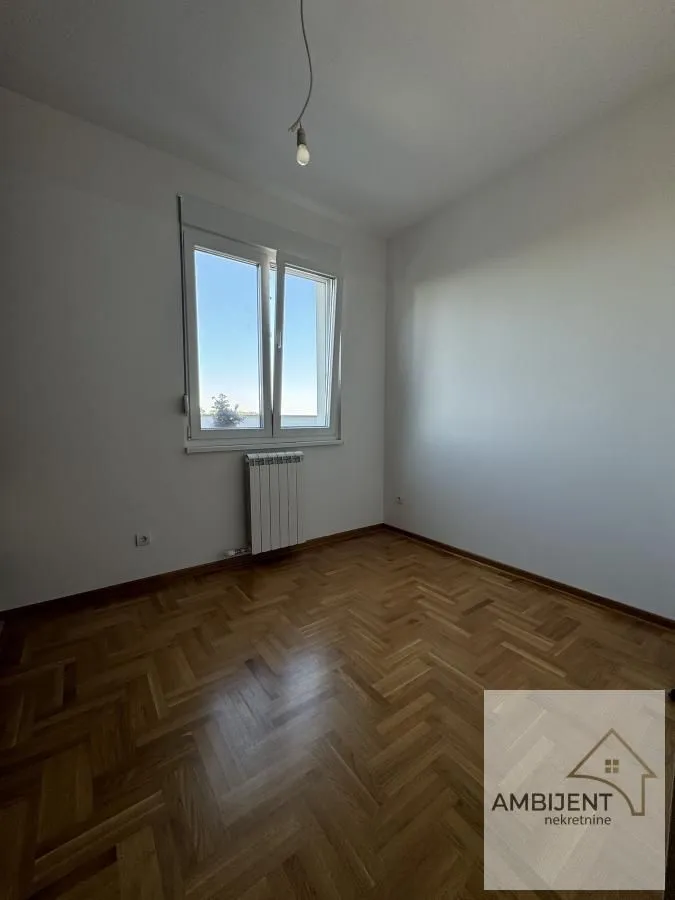 Prazna soba sa parketom i jednim prozorom.