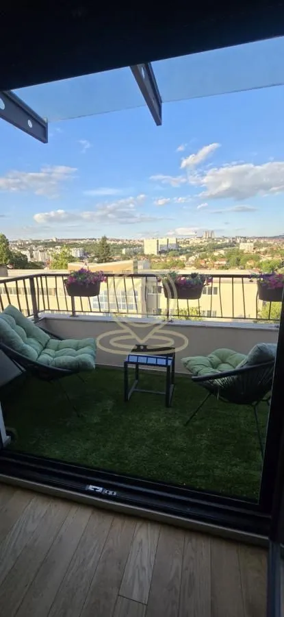 Namešten balkon sa veštačkom travom i pogledom na grad.