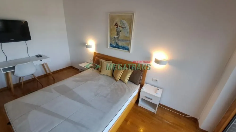 Nameštena spavaća soba sa bračnim krevetom, radnim stolom i televizorom.