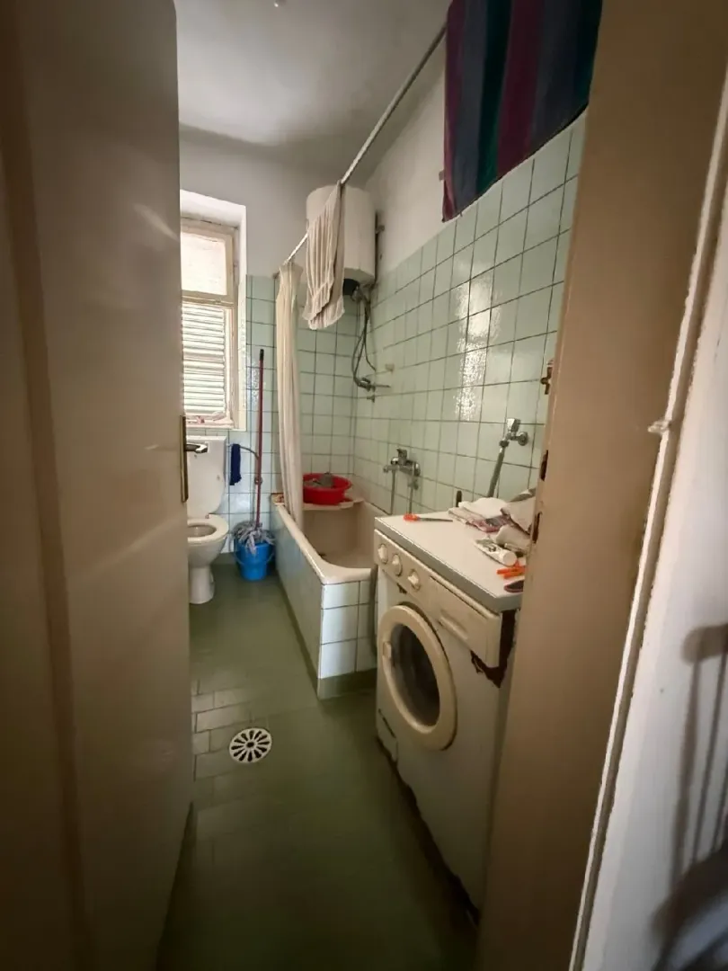 Starije kupatilo sa kadom, wc šoljom i veš mašinom.
