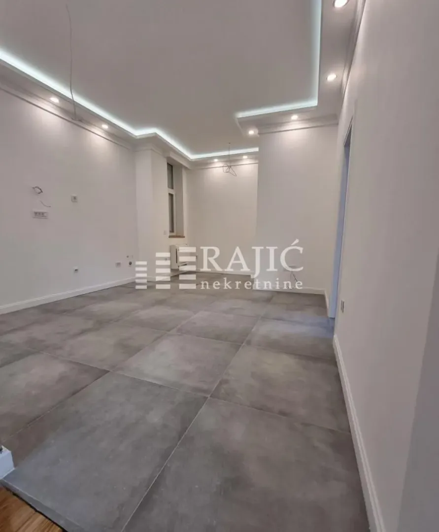 Empty room with grey floor tiles and a dropped ceiling with lighting.