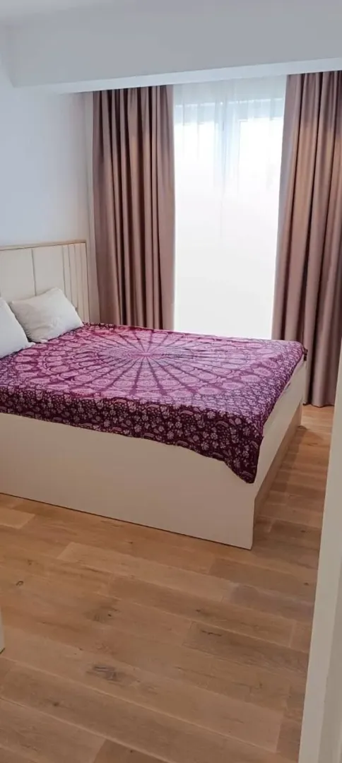 Namještena spavaća soba sa bračnim krevetom i prozorom sa zavjesama.