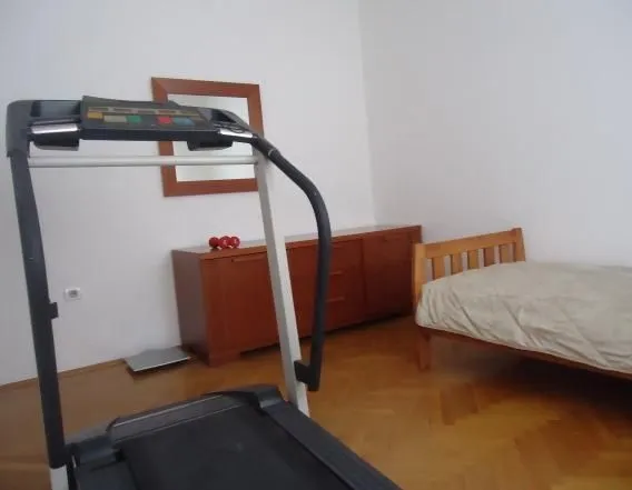 A simple bedroom featuring a wooden bed, dresser, and a treadmill.