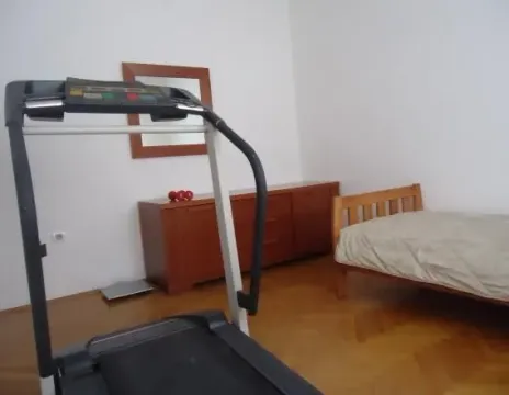 A simple bedroom featuring a wooden bed, dresser, and a treadmill. - image 7