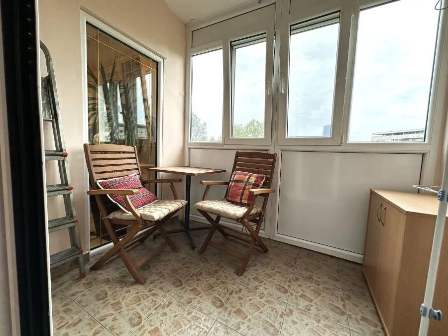 Enclosed balcony with a wooden table, chairs, and tiled flooring.