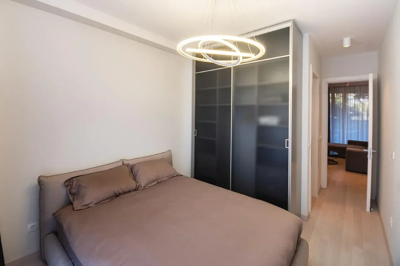 Namještena spavaća soba sa bračnim krevetom, garderoberom i modernim lusterom.
