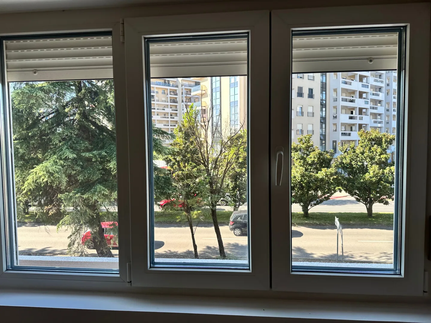 Pogled kroz prozor na okolne zgrade i zelenilo.