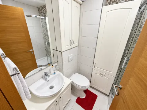Manje kupatilo sa umivaonikom, WC šoljom, tuš kabinom i bijelim ormarićima. - image 9