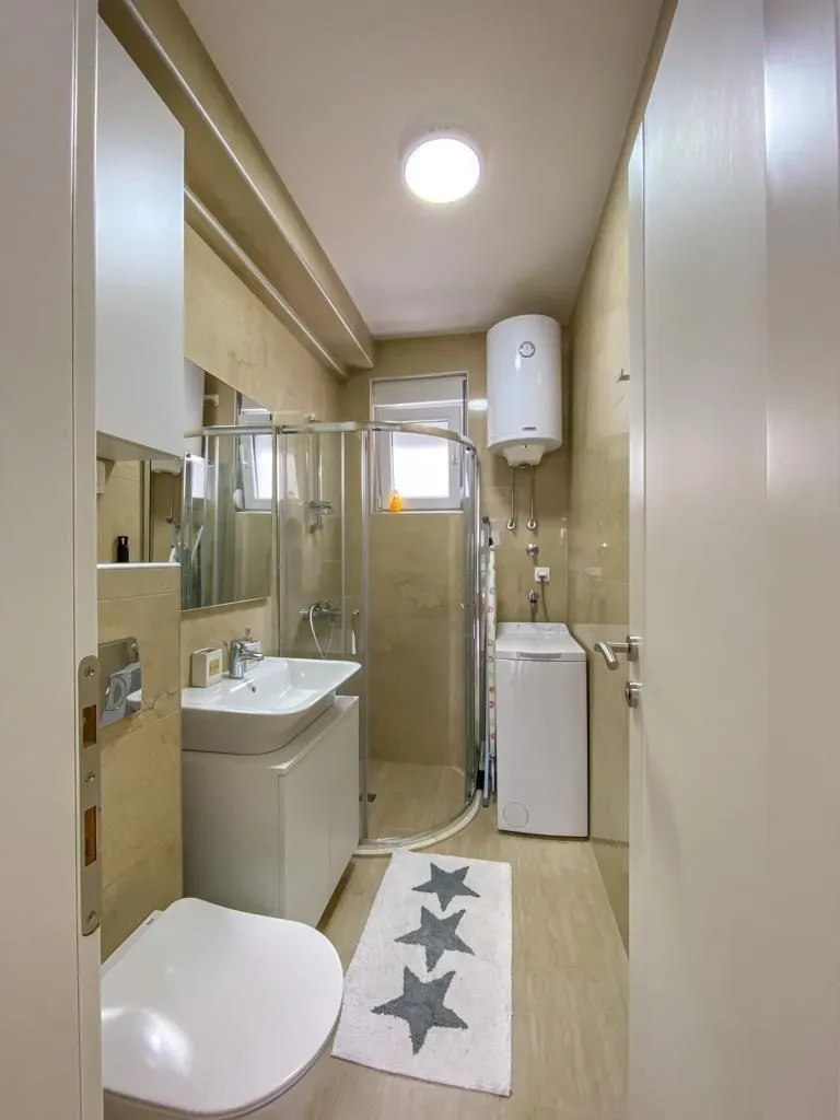 Compact bathroom with a shower cabin, sink, toilet, and washing machine.