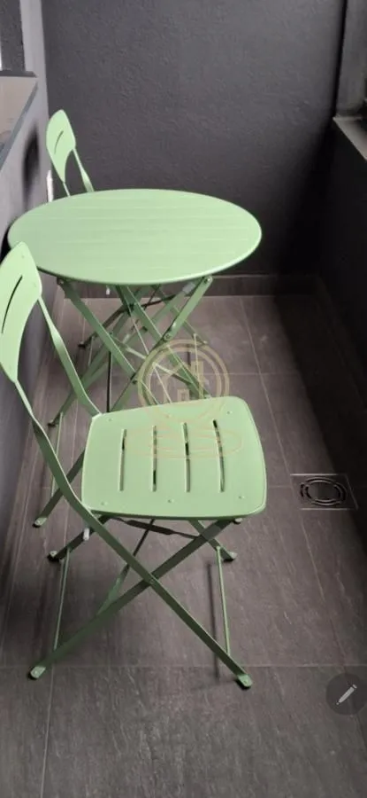 Small balcony with a table and green folding chairs.