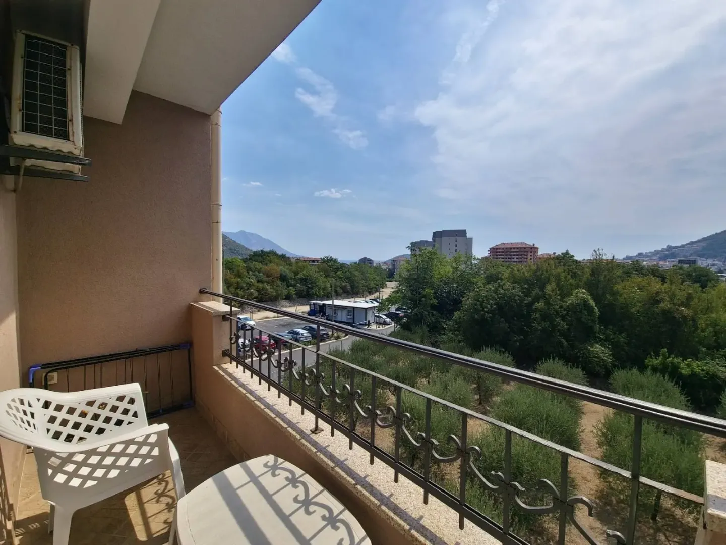 Small furnished balcony with a view of greenery and surrounding buildings.