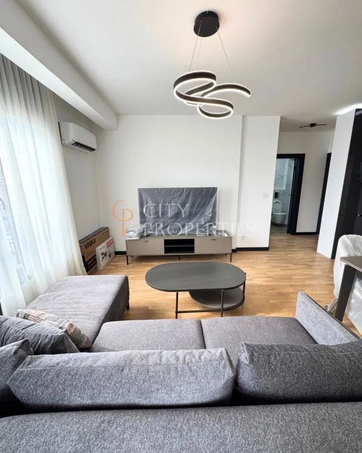 Namještena dnevna soba sa ugaonom garniturom, televizorom i modernim lusterom.