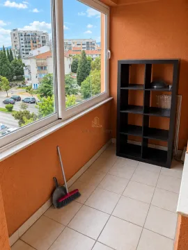 Glazed balcony with a black shelving unit, a broom, and a view of surrounding buildings and street. - image 7