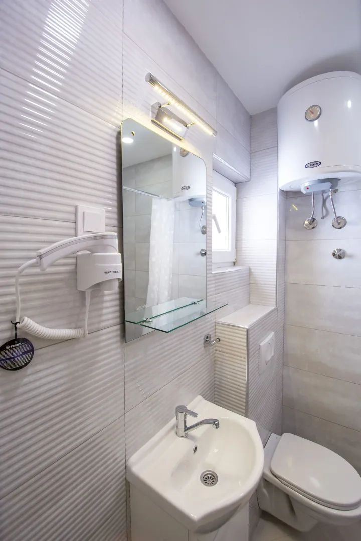 Smaller bathroom with a sink, mirror, water heater, and toilet.