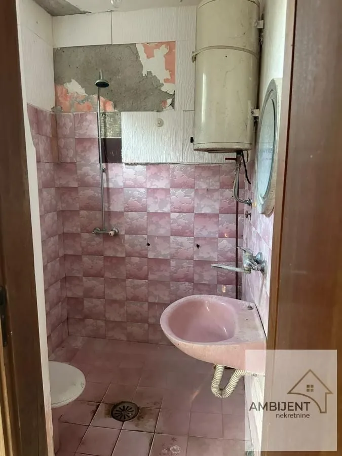 Starije kupatilo sa roze pločicama, umivaonikom i bojlerom.