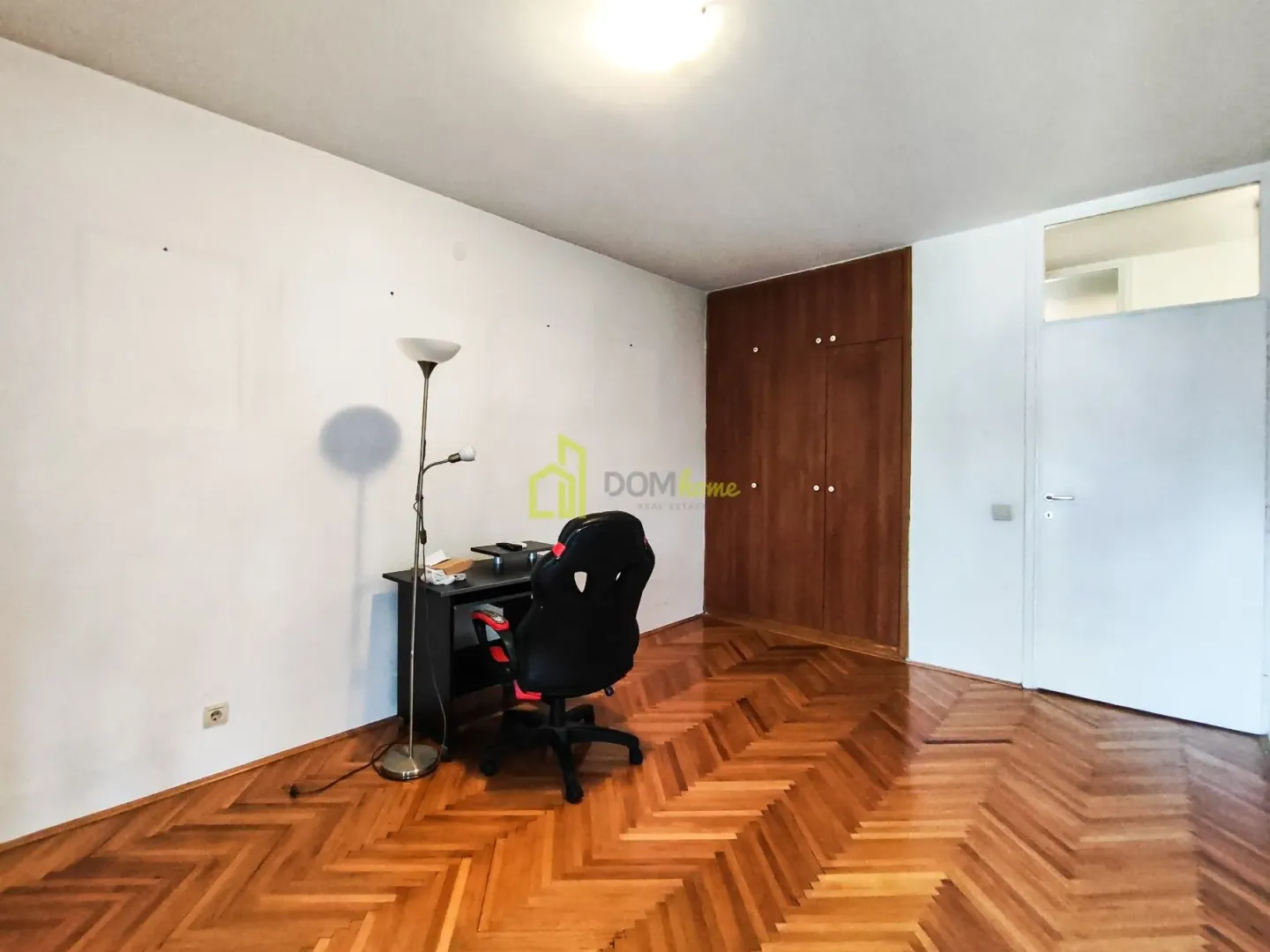 Soba sa radnim stolom, kancelarijskom stolicom i drvenim ormarom.