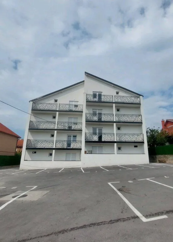 Spoljašnji izgled stambene zgrade sa parkingom ispred.