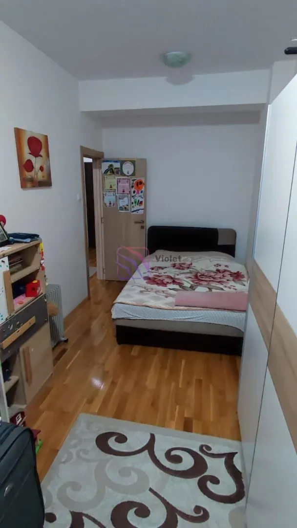 Namještena spavaća soba sa bračnim krevetom, ormarom i drvenim podom.