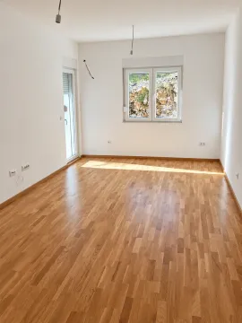 Prazna soba sa bijelim zidovima, drvenim parketom, prozorom i balkonskim vratima. - image 3