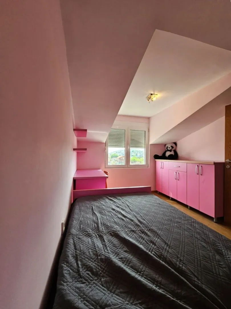 Dječja soba u potkrovlju sa krevetom i roze namještajem.