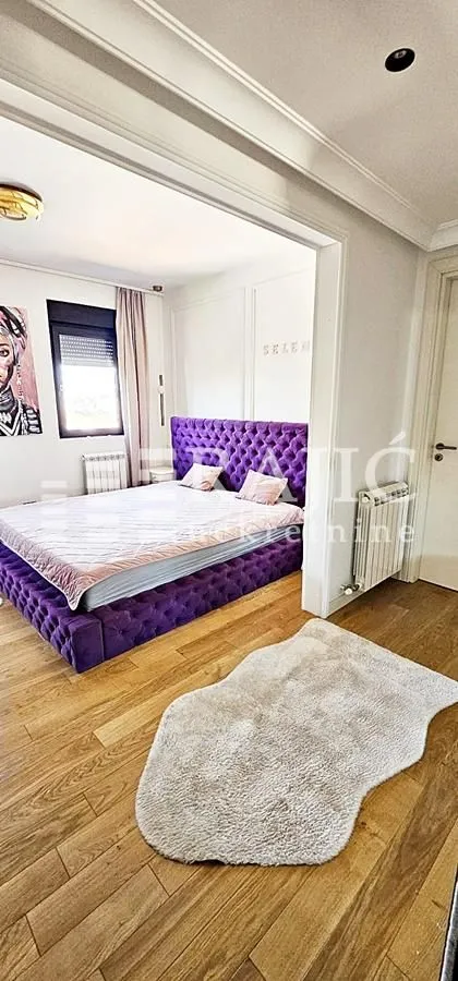 Furnished bedroom with a large purple bed and hardwood flooring.