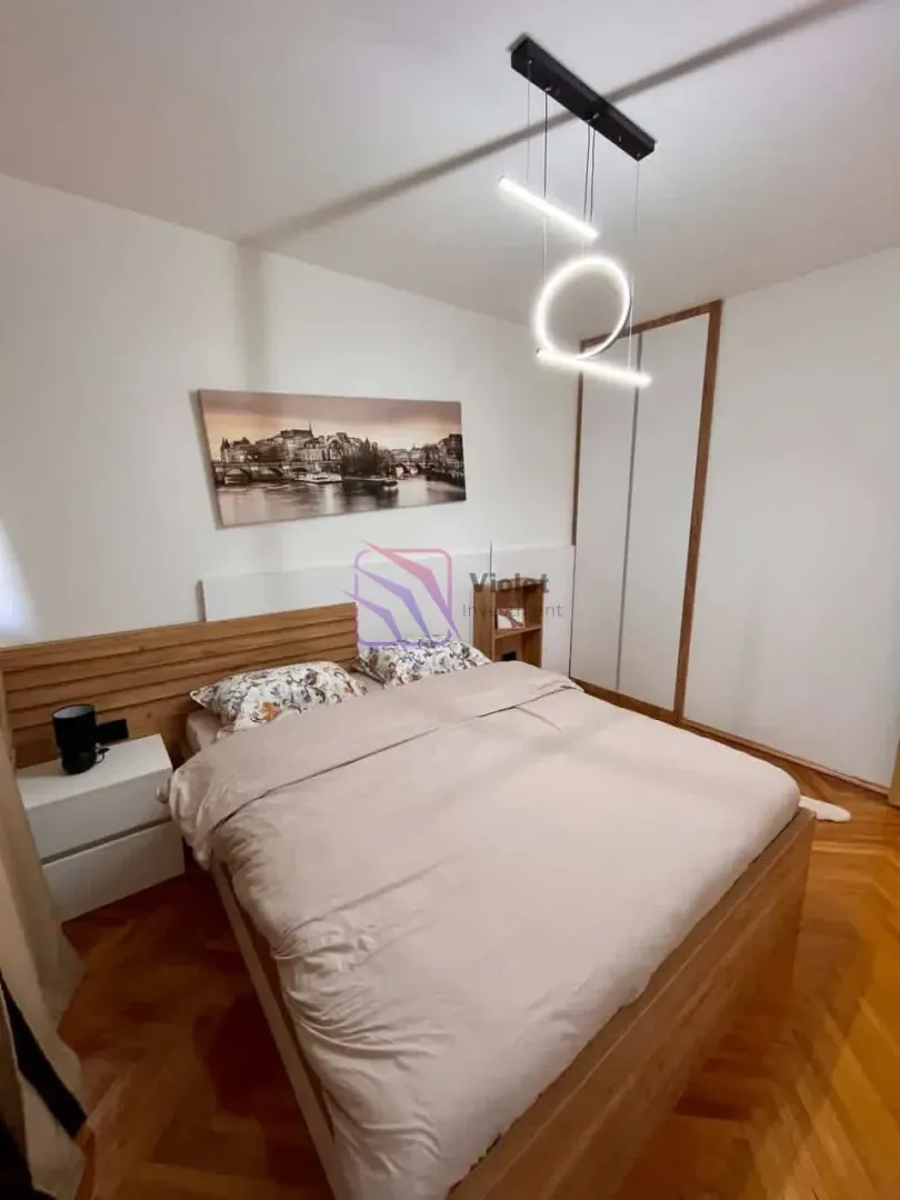 Namještena spavaća soba sa bračnim krevetom, plakarom i drvenim podom.
