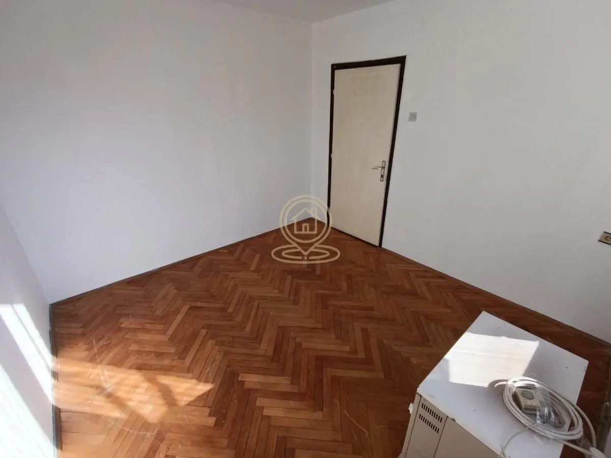 Prazna soba sa parketom i belim zidovima.