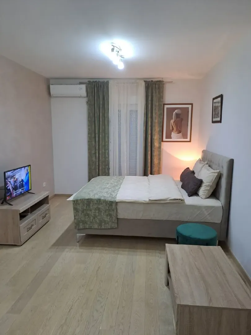 Furnished bedroom with a double bed, TV unit, and a window with curtains.