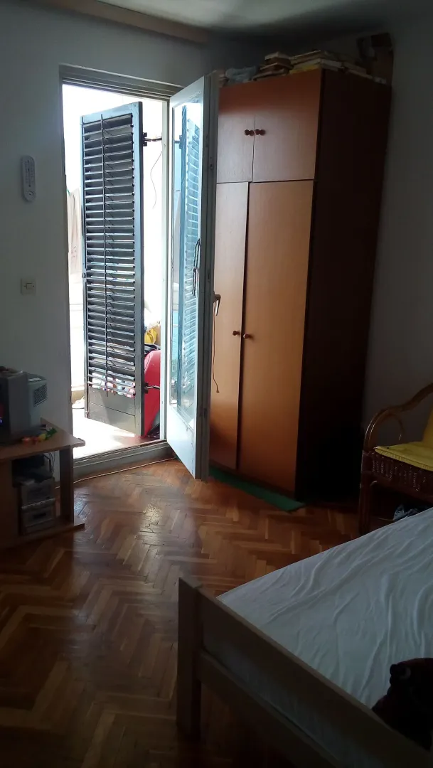 Spavaća soba sa drvenim ormarom, krevetom i izlazom na terasu.