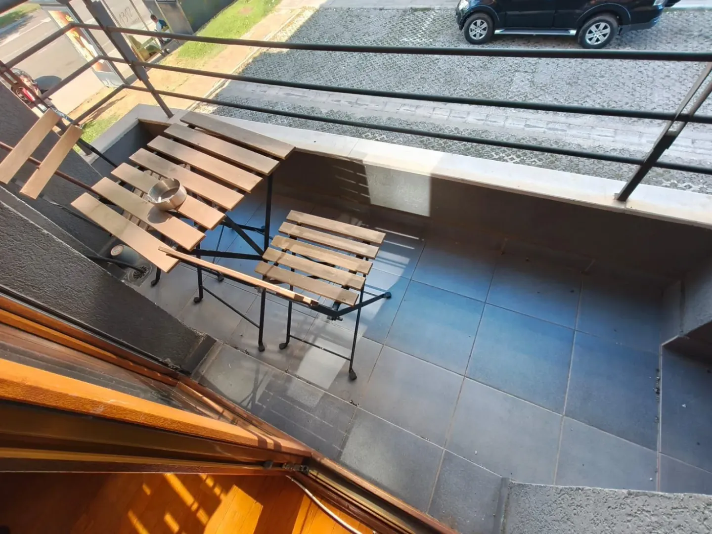 Small tiled balcony with a wooden table and chairs and a metal railing.
