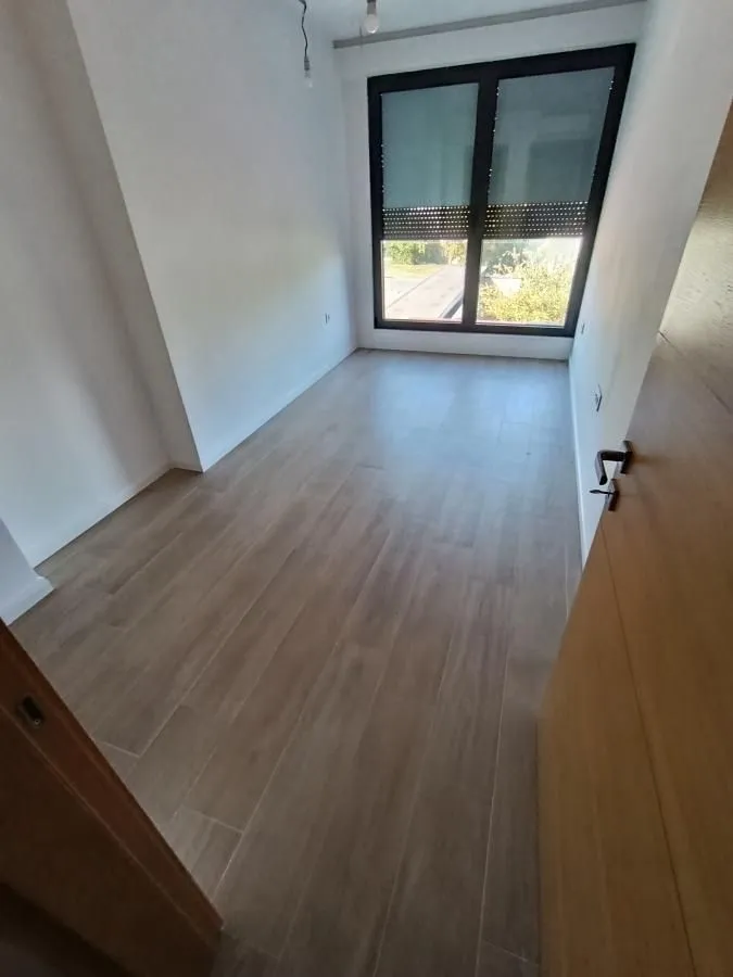 Empty room with light walls, wooden flooring, and a window.