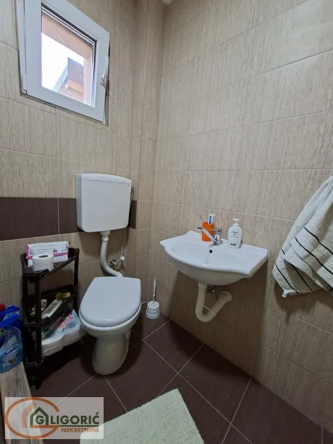 Manje kupatilo obloženo keramičkim pločicama sa WC šoljom i umivaonikom.