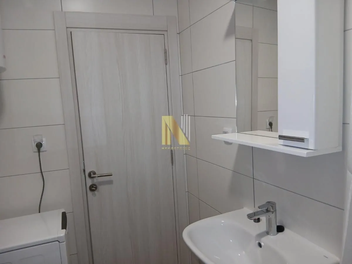 Manje kupatilo sa umivaonikom, ogledalom i belim pločicama.