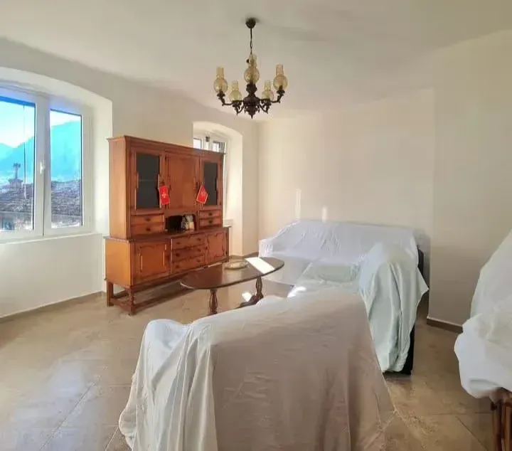 Living room with furniture covered in slipcovers and a wooden chest of drawers.