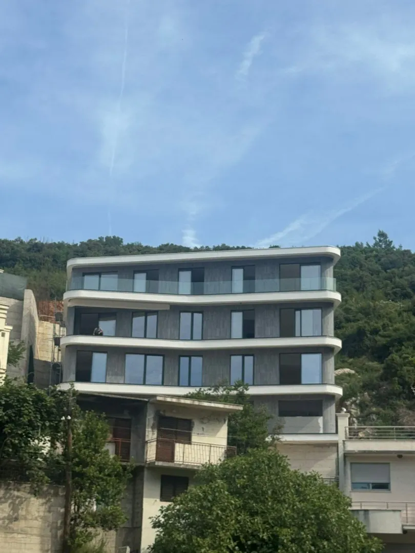 Exterior of a modern apartment building with balconies and greenery in the background.