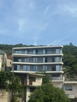 Exterior of a modern apartment building with balconies and greenery in the background. - image 12