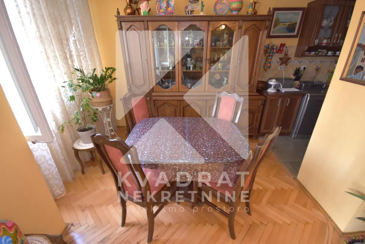 Trpezarija sa drvenim stolom, stolicama i velikom vitrinom.