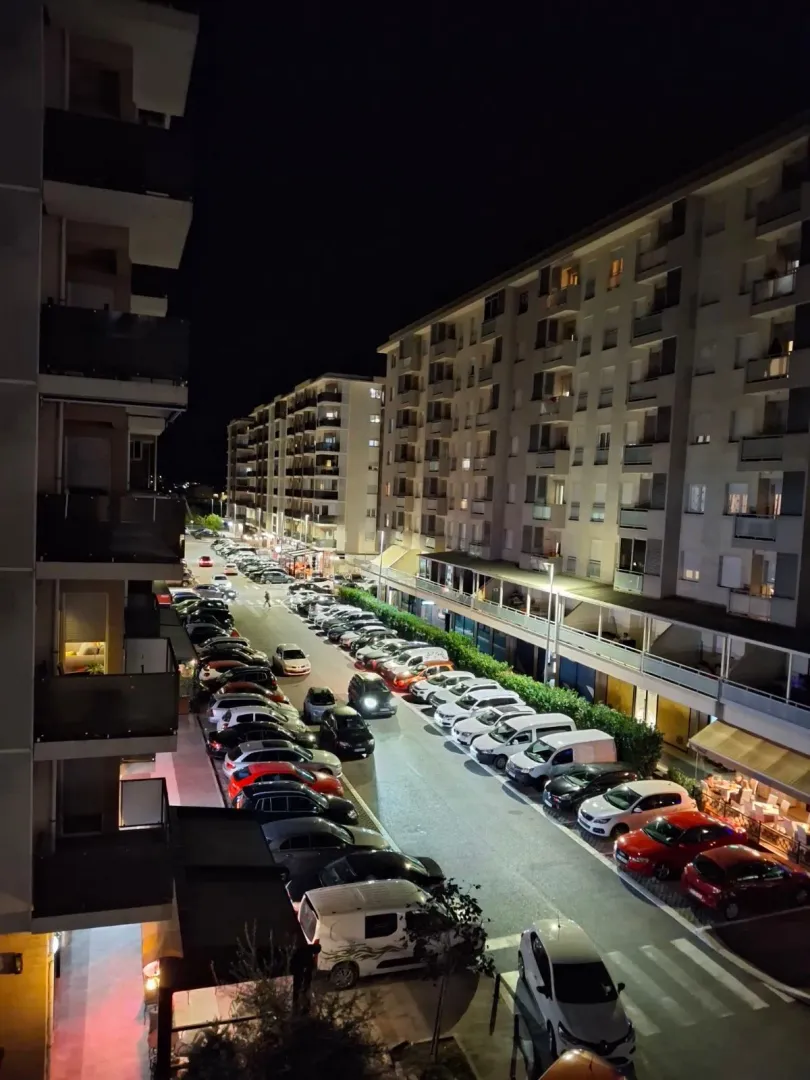 Night view of a street with parked cars and surrounding residential buildings.