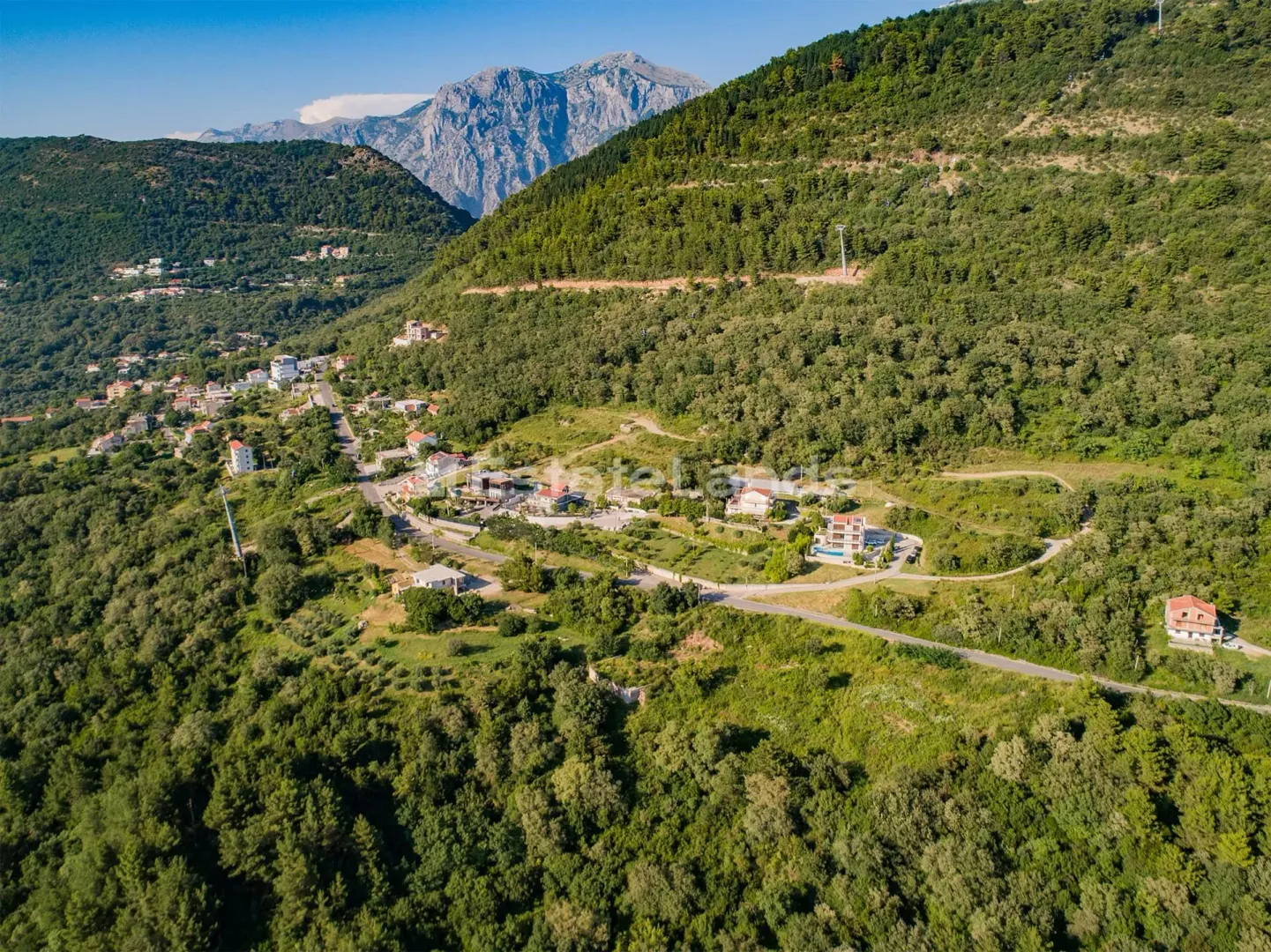 Pogled iz vazduha na okolno naselje i brda u pozadini.