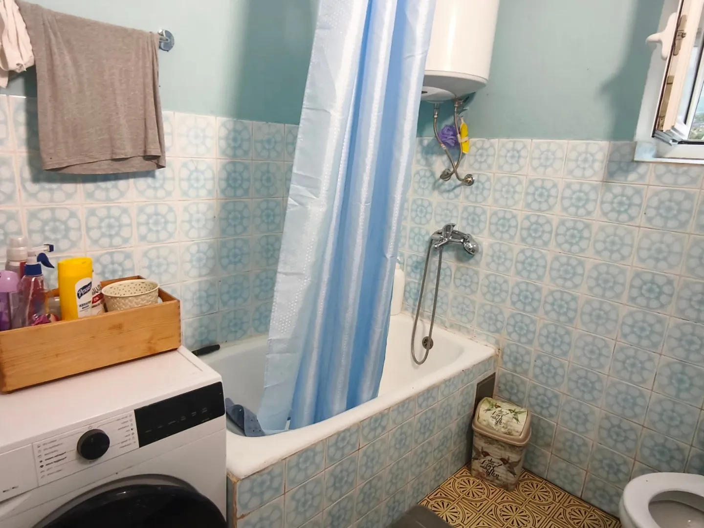 Small equipped bathroom with a bathtub, blue curtain, and washing machine.