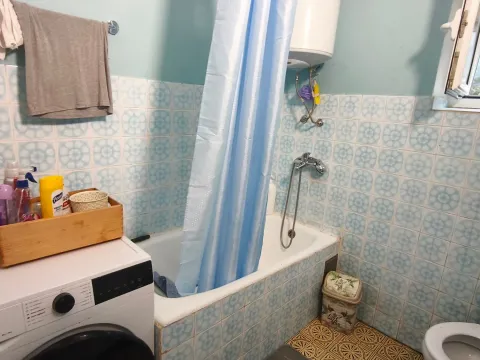 Small equipped bathroom with a bathtub, blue curtain, and washing machine. - image 11