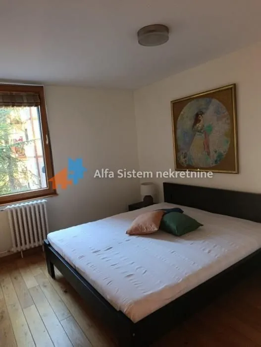 Nameštena spavaća soba sa bračnim krevetom, prozorom i slikom na zidu.