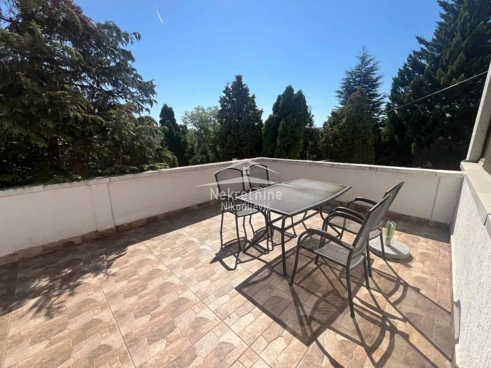 Spacious terrace with patio furniture and a view of greenery.