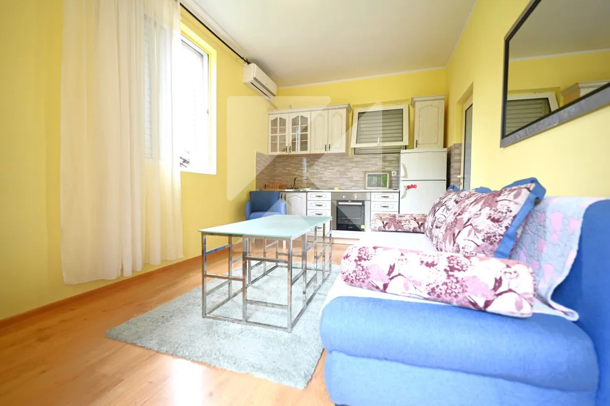 Living room with a sofa set and a built-in kitchen in the background.